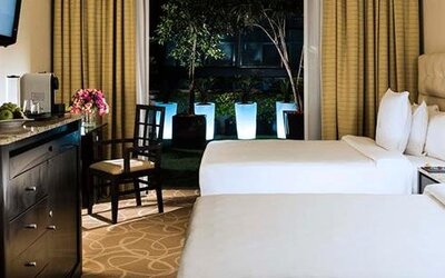 Guest room at Hotel Marquis Reforma featuring two beds, a work desk and floor-to-ceiling windows overlooking an outdoor area.
