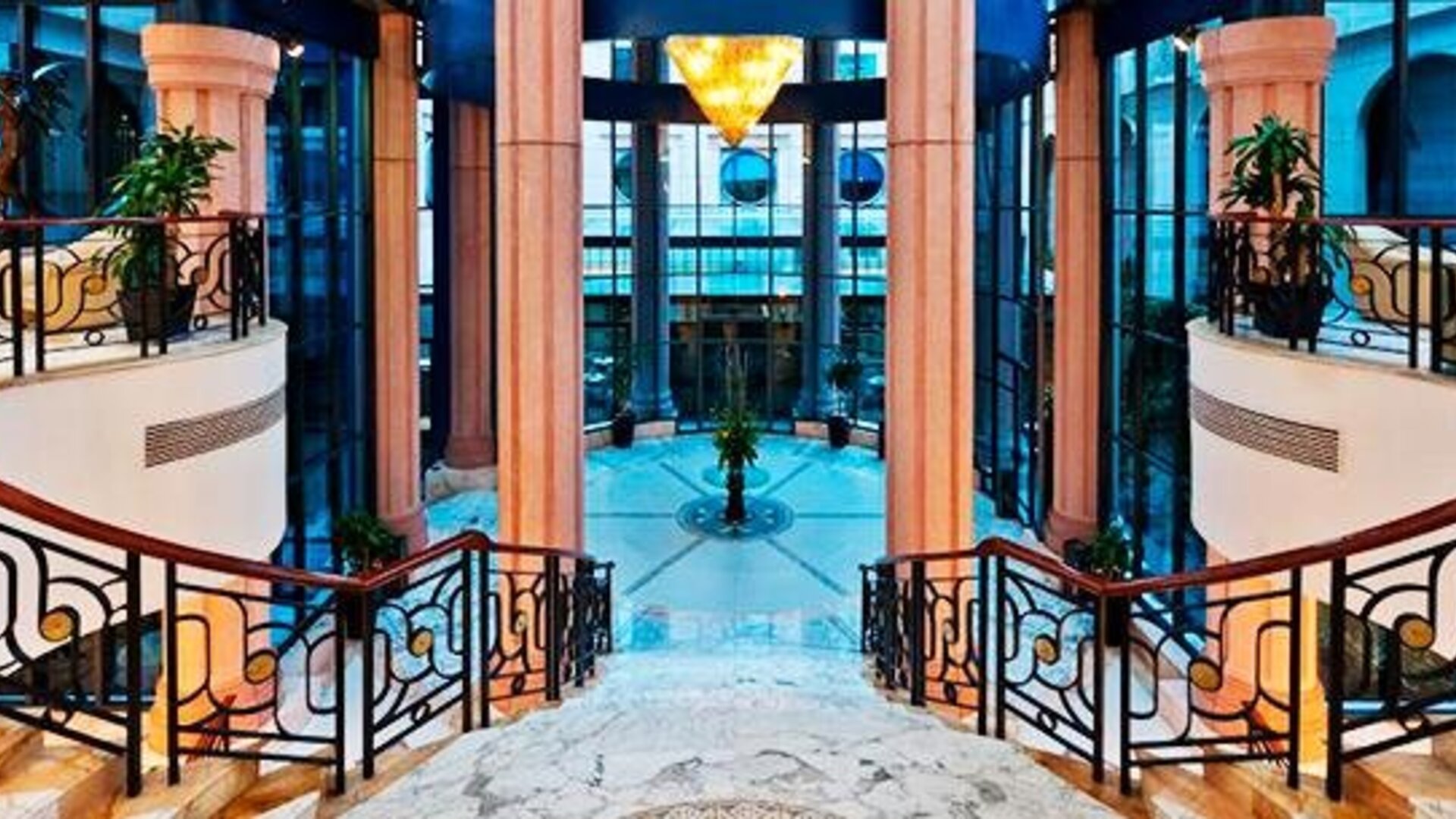 Grand interior staircase at Hotel Marquis Reforma featuring curved railings, marble finishes and a glass atrium.