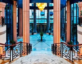 Grand interior staircase at Hotel Marquis Reforma featuring curved railings, marble finishes and a glass atrium.