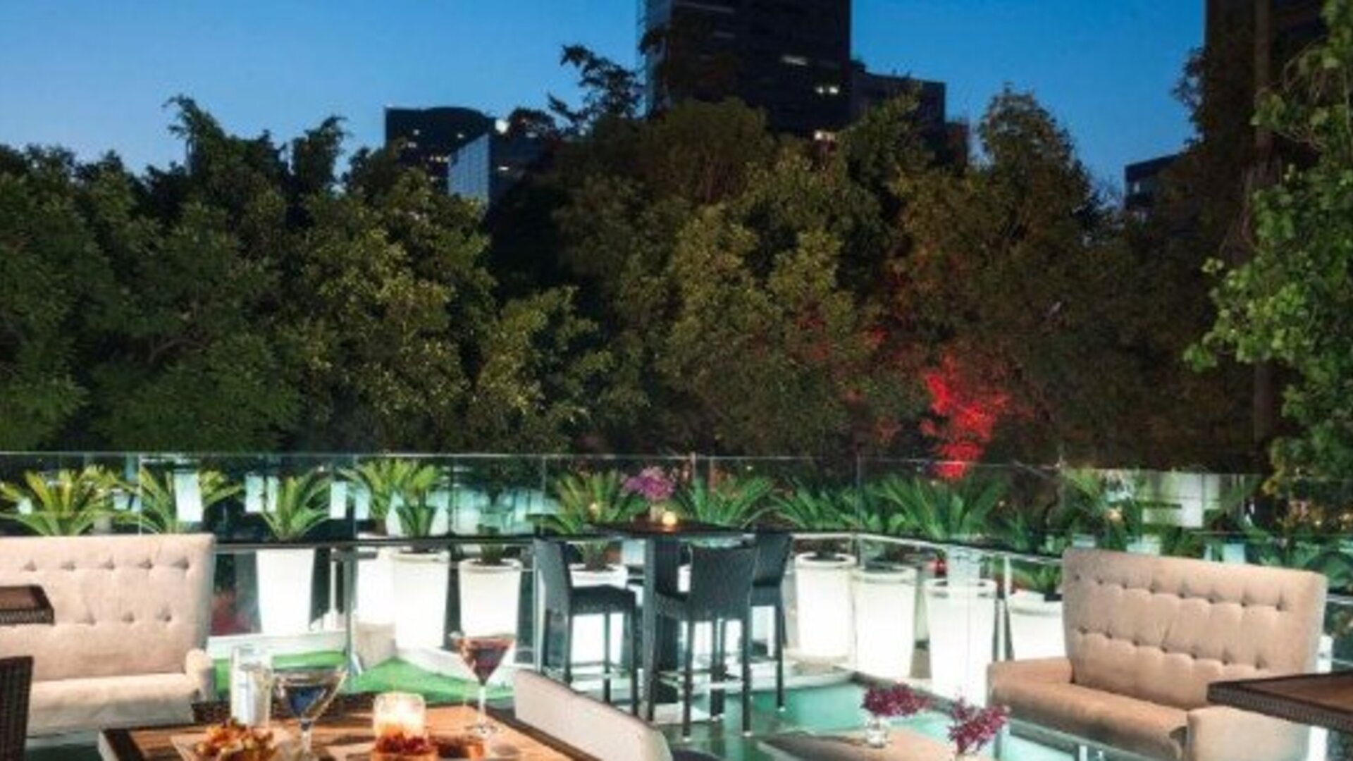 Outdoor terrace at Hotel Marquis Reforma featuring dining tables, lounge seating and views of surrounding greenery.