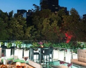 Outdoor terrace at Hotel Marquis Reforma featuring dining tables, lounge seating and views of surrounding greenery.