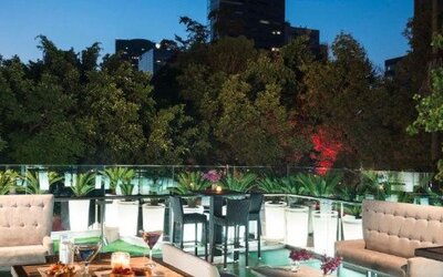 Outdoor terrace at Hotel Marquis Reforma featuring dining tables, lounge seating and views of surrounding greenery.