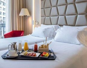 Guest room featuring a large bed, breakfast tray, red accent chair and natural light from the balcony doors at NH Collection Barcelona Pódium.