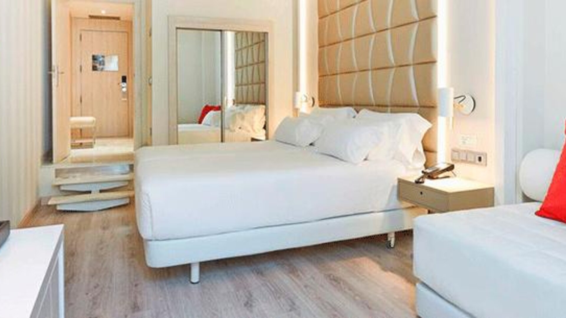 Bright guest room featuring a large bed, sofa, red accent cushion and contemporary furnishings at NH Collection Barcelona Pódium.