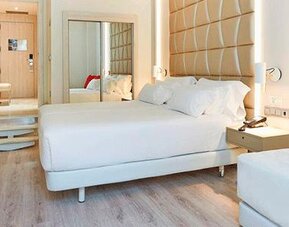 Bright guest room featuring a large bed, sofa, red accent cushion and contemporary furnishings at NH Collection Barcelona Pódium.