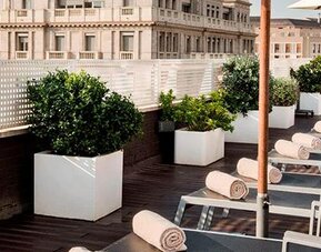 Rooftop terrace featuring sun loungers, umbrellas, planters and city views at NH Collection Barcelona Pódium.