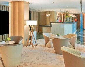 Elegant lobby seating area featuring modern armchairs, small tables and floor lamps at NH Collection Barcelona Pódium.