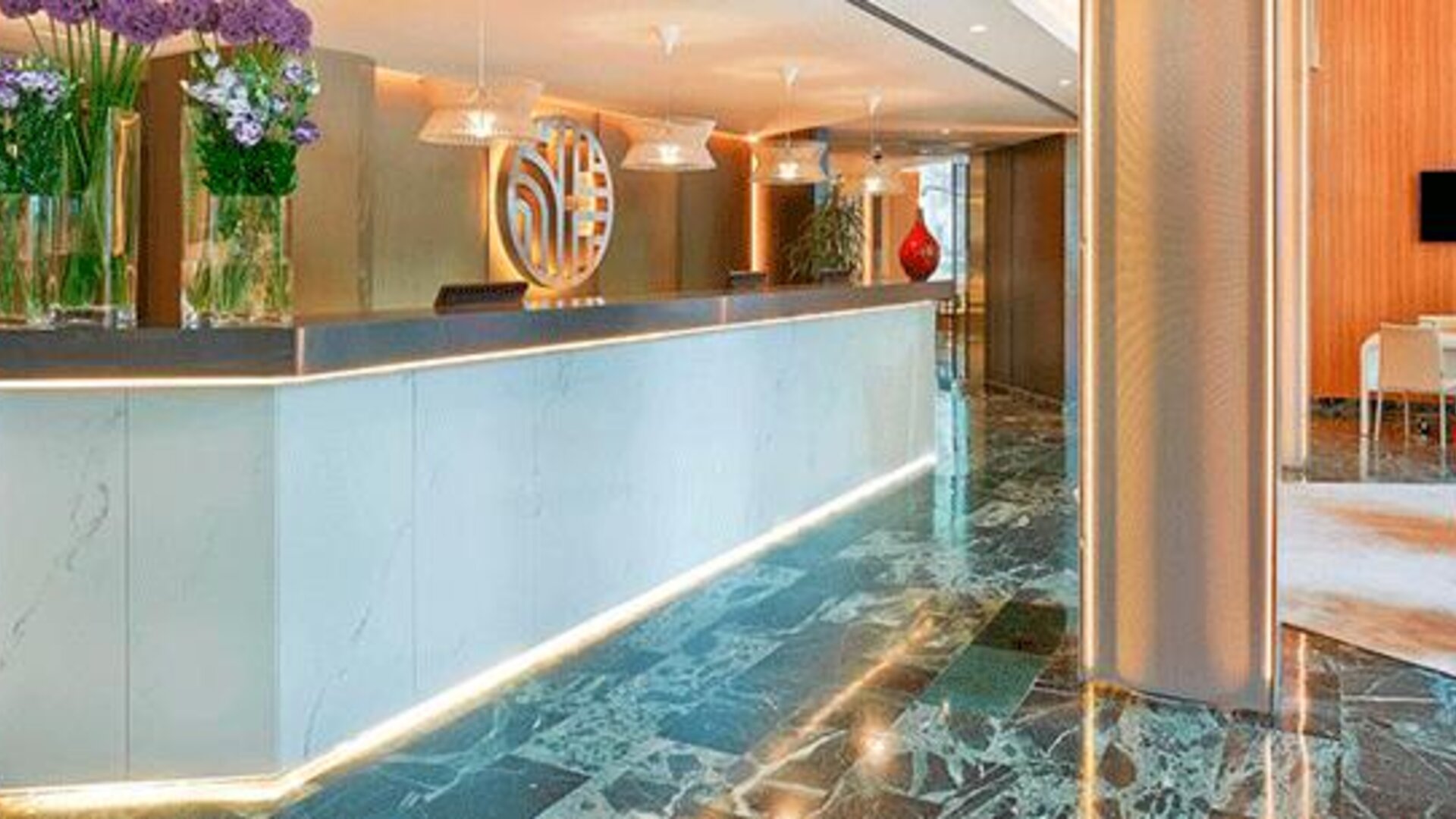 Contemporary reception desk featuring marble finishes, floral arrangements and warm lighting at NH Collection Barcelona Pódium.
