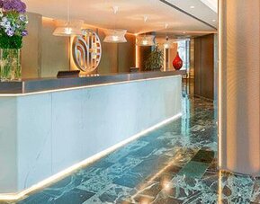 Contemporary reception desk featuring marble finishes, floral arrangements and warm lighting at NH Collection Barcelona Pódium.
