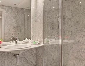 Marble bathroom featuring a sink, large mirror and glass-enclosed shower at NH Collection Barcelona Pódium.