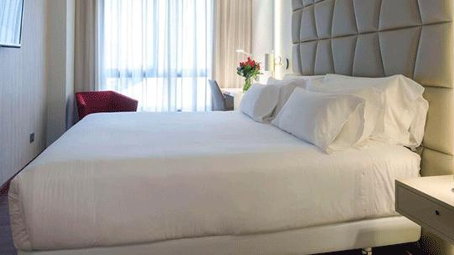 Modern guest room featuring a large bed, upholstered headboard, bedside lighting and natural light at NH Collection Barcelona Pódium.