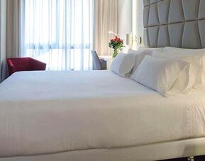 Modern guest room featuring a large bed, upholstered headboard, bedside lighting and natural light at NH Collection Barcelona Pódium.