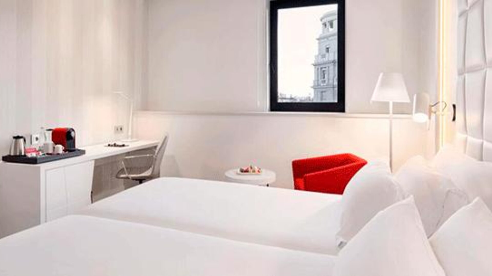 Bright twin guest room featuring two beds, a work desk, seating area and large window at NH Collection Barcelona Pódium.