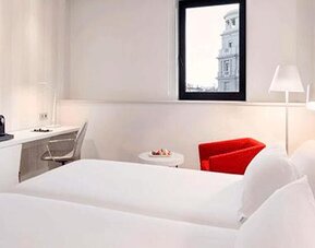 Bright twin guest room featuring two beds, a work desk, seating area and large window at NH Collection Barcelona Pódium.