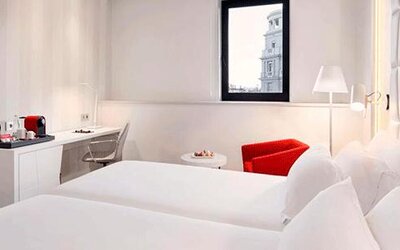 Bright twin guest room featuring two beds, a work desk, seating area and large window at NH Collection Barcelona Pódium.