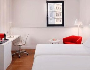 Contemporary guest room featuring two beds, a work desk, red accent chair and wall-mounted television at NH Collection Barcelona Pódium.