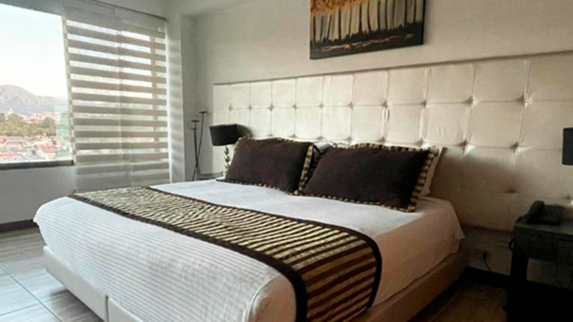 Spacious guest room featuring a king bed, seating area, polished wood flooring and large windows at Hotel Airport Travel.