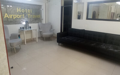 Lobby seating area featuring a black sofa, armchairs, large wall mirror and refreshment table at Hotel Airport Travel.