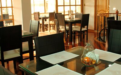 Bright dining area featuring glass-top tables, black chairs and large windows at Hotel Airport Travel.