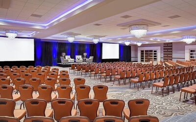 Spacious conference hall featuring theater-style seating, elegant chandeliers and a presentation stage at Sheraton Houston Brookhollow Hotel.