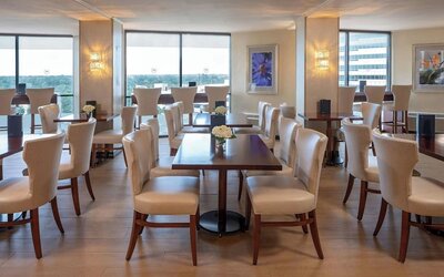 Bright dining area featuring floor-to-ceiling windows, upholstered seating and contemporary décor at Sheraton Houston Brookhollow Hotel.