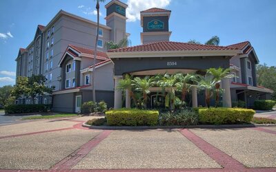 Modern hotel exterior featuring Mediterranean-inspired architecture, palm trees and a covered entrance at La Quinta Inn & Suites By Wyndham Orlando I Drive/Conv Ctr.