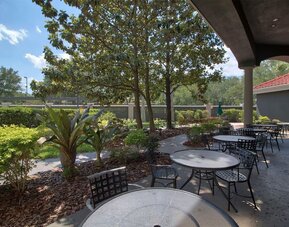 Landscaped outdoor terrace featuring shaded seating, garden views and casual dining tables at La Quinta Inn & Suites By Wyndham Orlando I Drive/Conv Ctr.