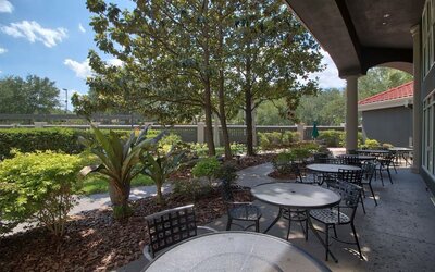 Landscaped outdoor terrace featuring shaded seating, garden views and casual dining tables at La Quinta Inn & Suites By Wyndham Orlando I Drive/Conv Ctr.