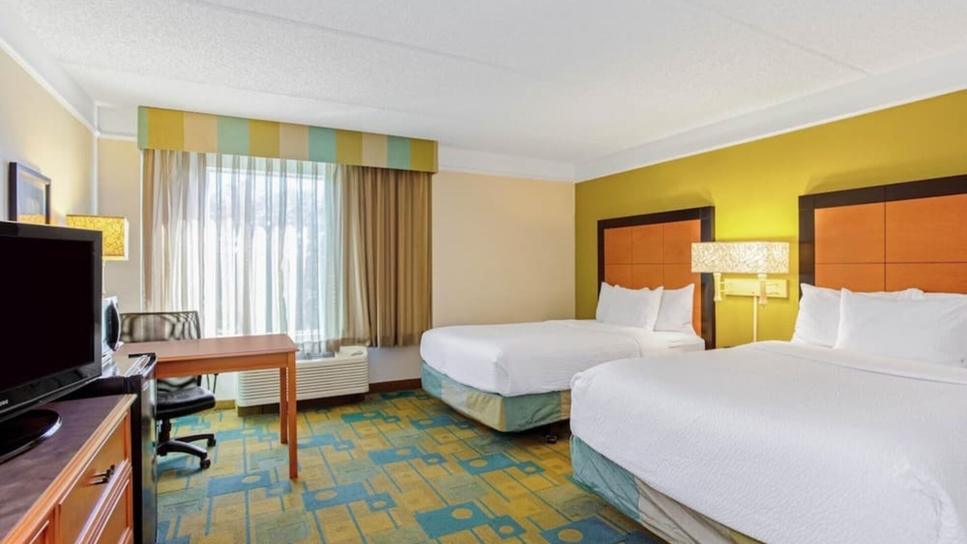 Bright guest room featuring two double beds, a dedicated workspace and large windows with natural light at La Quinta Inn & Suites By Wyndham Orlando I Drive/Conv Ctr.