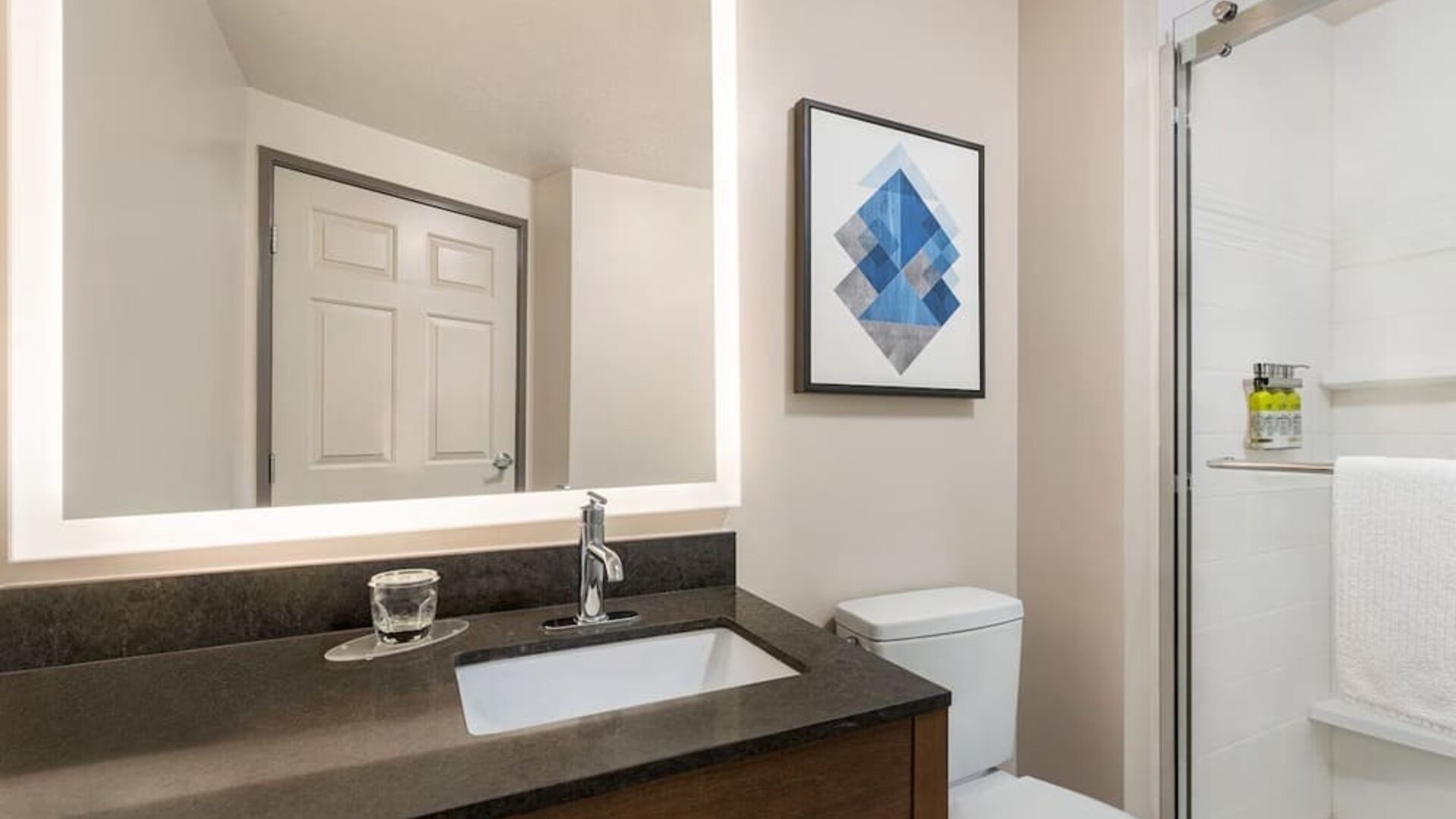 Contemporary bathroom featuring a walk-in glass shower, an illuminated vanity mirror and modern finishes at Candlewood Suites Meridian.