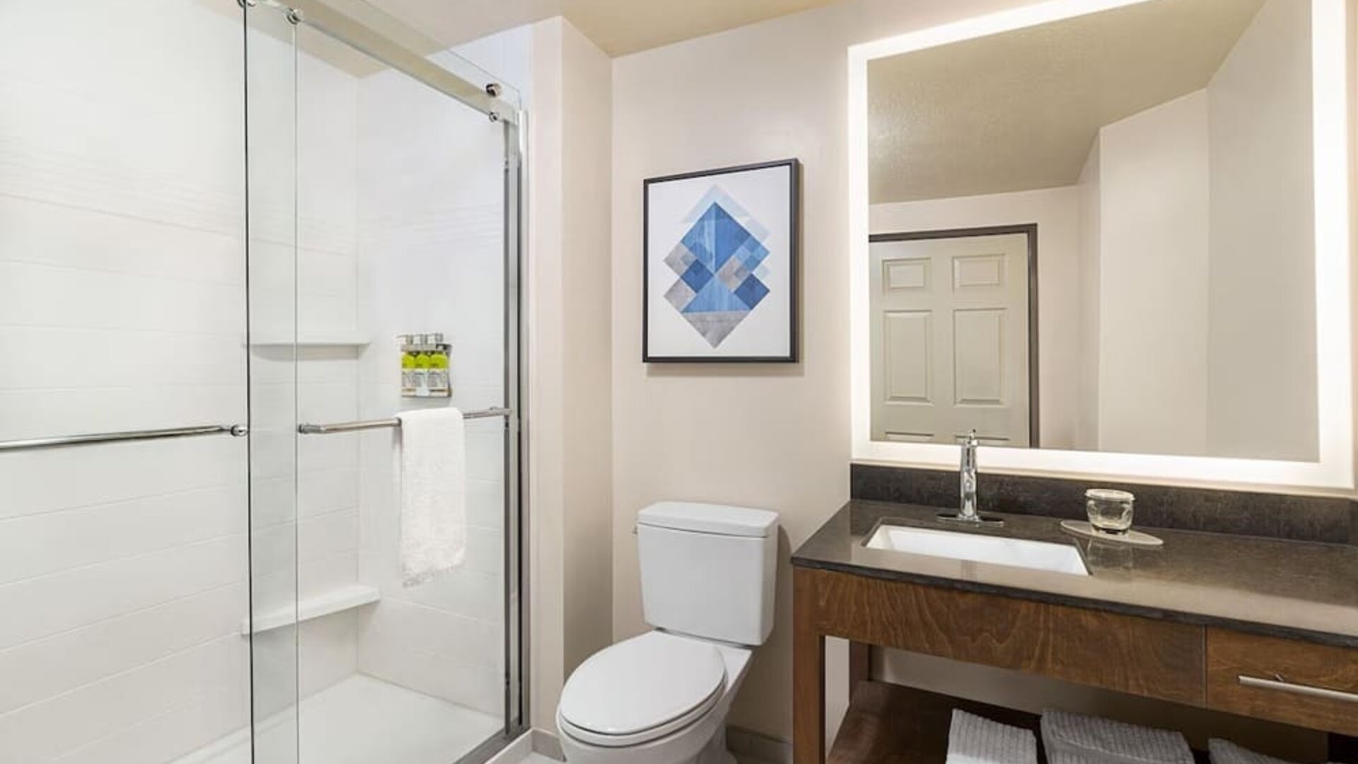 Modern bathroom featuring a spacious vanity, a glass-enclosed shower and neatly arranged towels at Candlewood Suites Meridian.