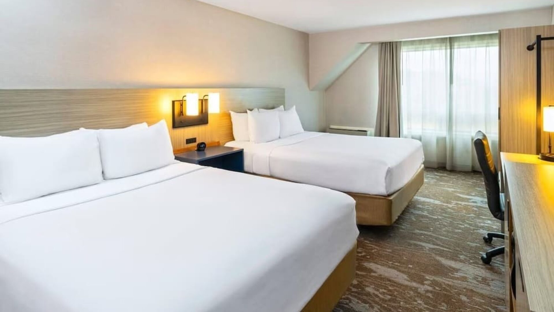 Spacious guest room featuring two beds, a work area and large windows with natural light at Comfort Inn Truro.