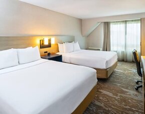 Spacious guest room featuring two beds, a work area and large windows with natural light at Comfort Inn Truro.