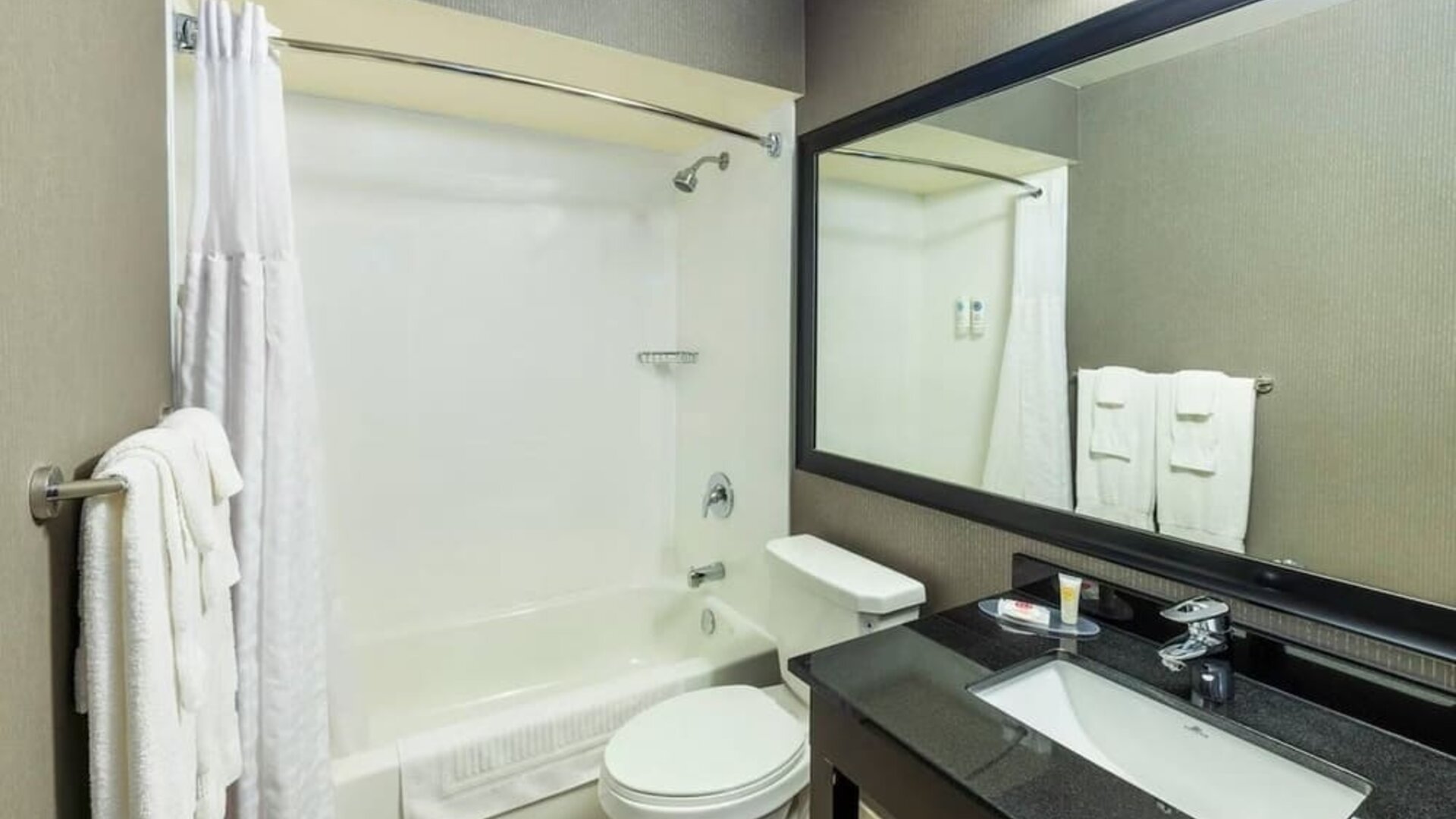Modern bathroom featuring a tub and shower combination, a granite vanity and a large framed mirror at Comfort Inn Truro.