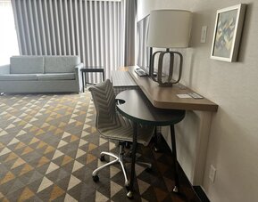 In-room workspace featuring a large desk, ergonomic seating and a comfortable lounge area with floor-to-ceiling window coverings at Holiday Inn Toronto Airport East.