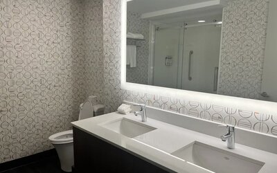 Modern hotel bathroom featuring a double vanity, illuminated mirror and an accessible walk-in shower at Holiday Inn Toronto Airport East.