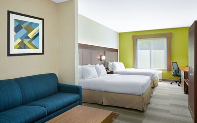Guest room featuring two beds, a sofa, a work desk and modern décor designed for comfort at Holiday Inn Express & Suites Ontario.
