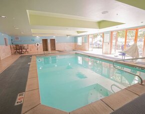 Indoor pool area featuring a spacious swimming pool, accessible features and comfortable seating at Holiday Inn Express & Suites Ontario.