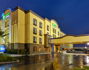 Evening exterior view featuring illuminated architecture, a covered porte cochère and a welcoming entrance at Holiday Inn Express SFO Airport North.