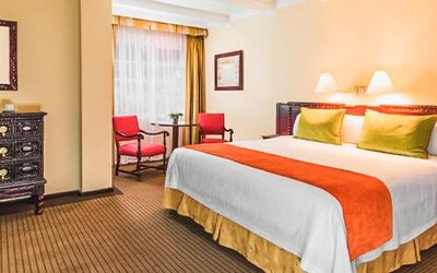 Guest room with one bed featuring handcrafted wood furniture, accent seating, bedside lamps, and classic interior design at Hotel Geneve.