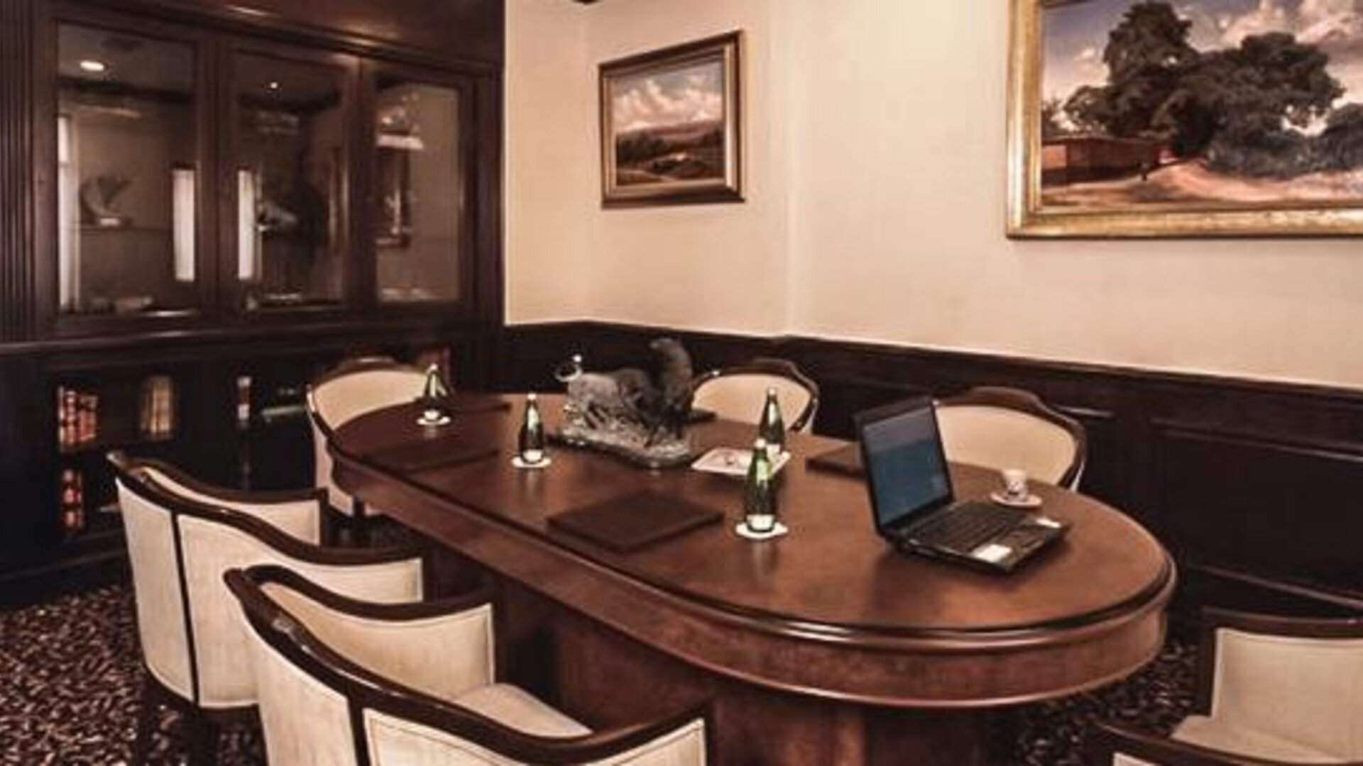 Executive boardroom featuring a large conference table, upholstered chairs, wood cabinetry, and workspace amenities at Hotel Geneve.