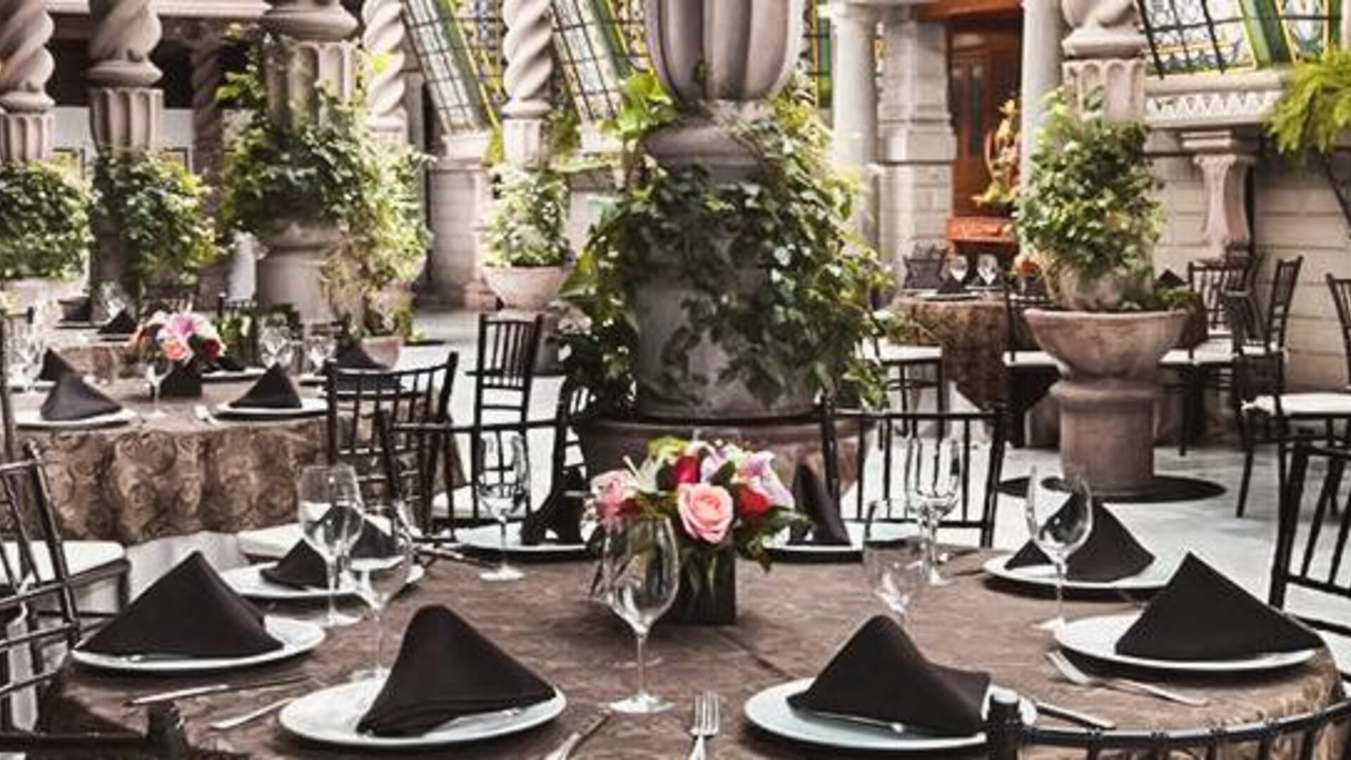 Dining area featuring round tables, formal place settings, decorative columns, plants, and an open atrium design at Hotel Geneve.