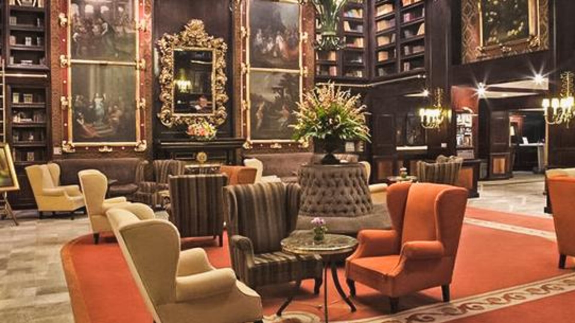 Grand lounge featuring dark wood décor, artwork, floor-to-ceiling bookshelves, and multiple seating areas at Hotel Geneve.