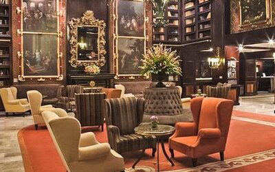 Grand lounge featuring dark wood décor, artwork, floor-to-ceiling bookshelves, and multiple seating areas at Hotel Geneve.