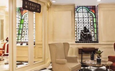 Lobby seating area adjacent to the barber shop featuring stained-glass windows, marble flooring, and comfortable armchairs at Hotel Geneve.