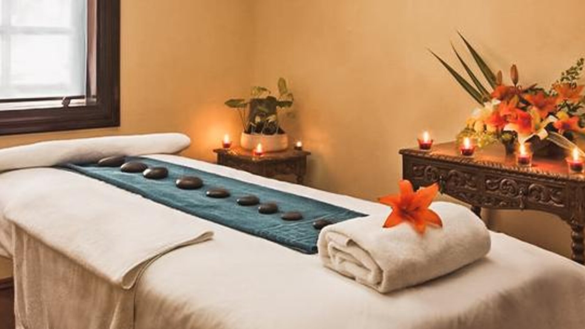 Spa treatment room featuring a massage table, decorative candles, floral arrangements, and a relaxing atmosphere at Hotel Geneve.