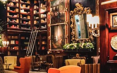 Library-style lounge with dark wood paneling, artwork, decorative displays, built-in bookshelves, and comfortable seating at Hotel Geneve.