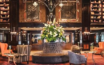 Spacious lobby featuring a central floral arrangement, floor-to-ceiling bookshelves, chandeliers, and multiple seating areas at Hotel Geneve.