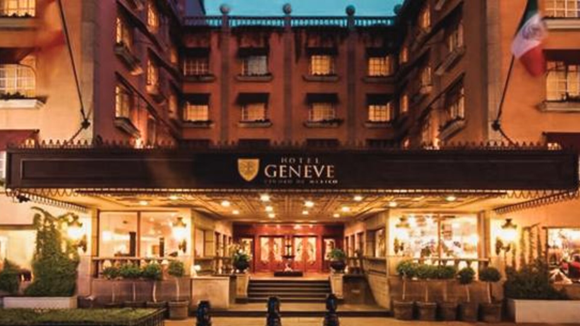 Exterior view of the grand entrance featuring the illuminated marquee, landscaped walkways, and traditional architectural details at Hotel Geneve.