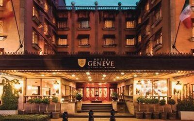 Exterior view of the grand entrance featuring the illuminated marquee, landscaped walkways, and traditional architectural details at Hotel Geneve.